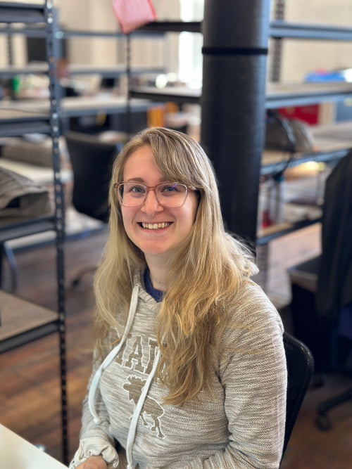 Kaitlynn, stitcher at C. Richard's, smiling at her workstation in the Lewiston, Maine workshop