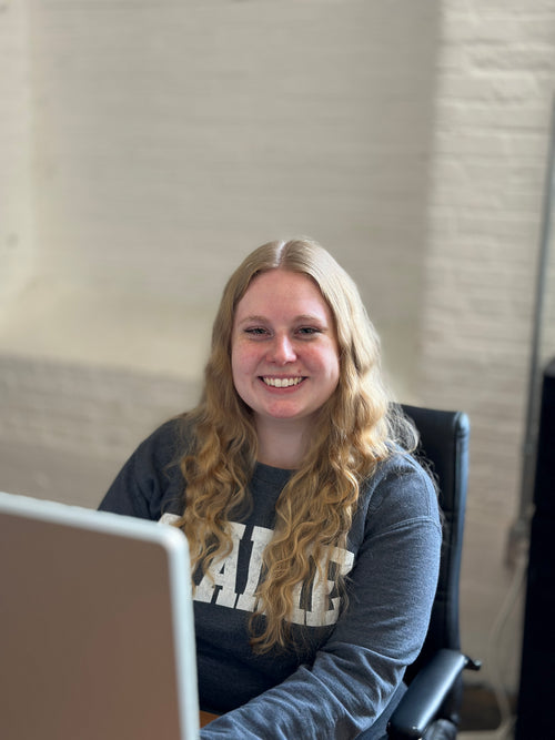 Allie, graphic designer at C. Richard's, smiling at her laptop in the workshop